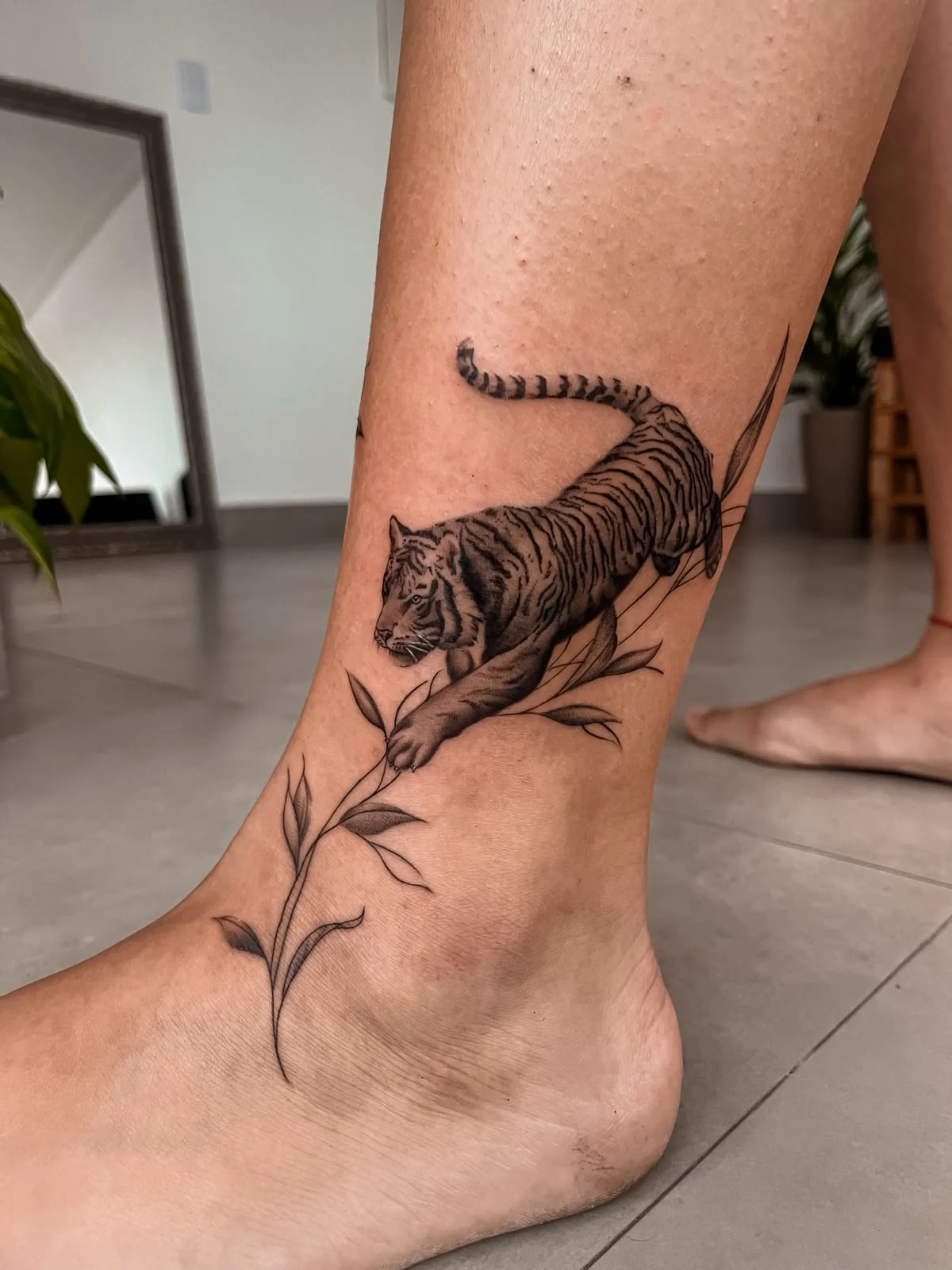 Tatuagem de tigre em preto e sombra integrada ao tornozelo, criada por Thay